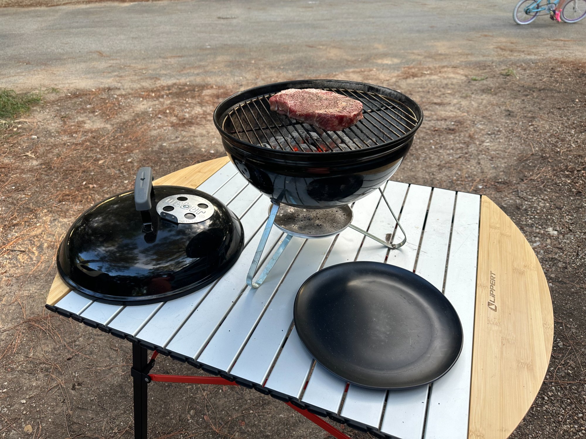 Lippert camping table being used as a cooking station with a small charcoal grill and steak
