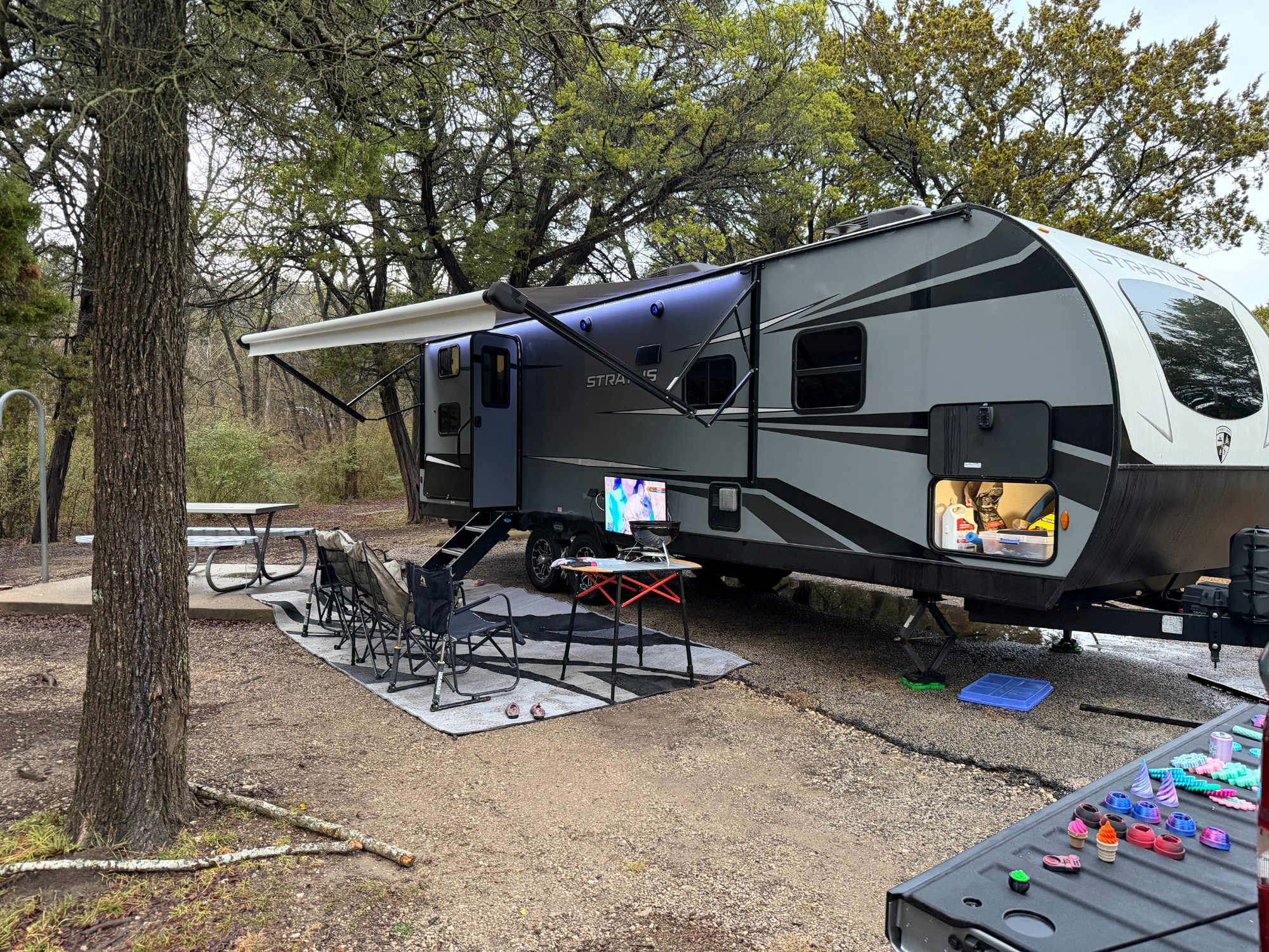 Venture Stratus SR281VBH set up at campsite with Lippert table, awning lights, and outdoor TV